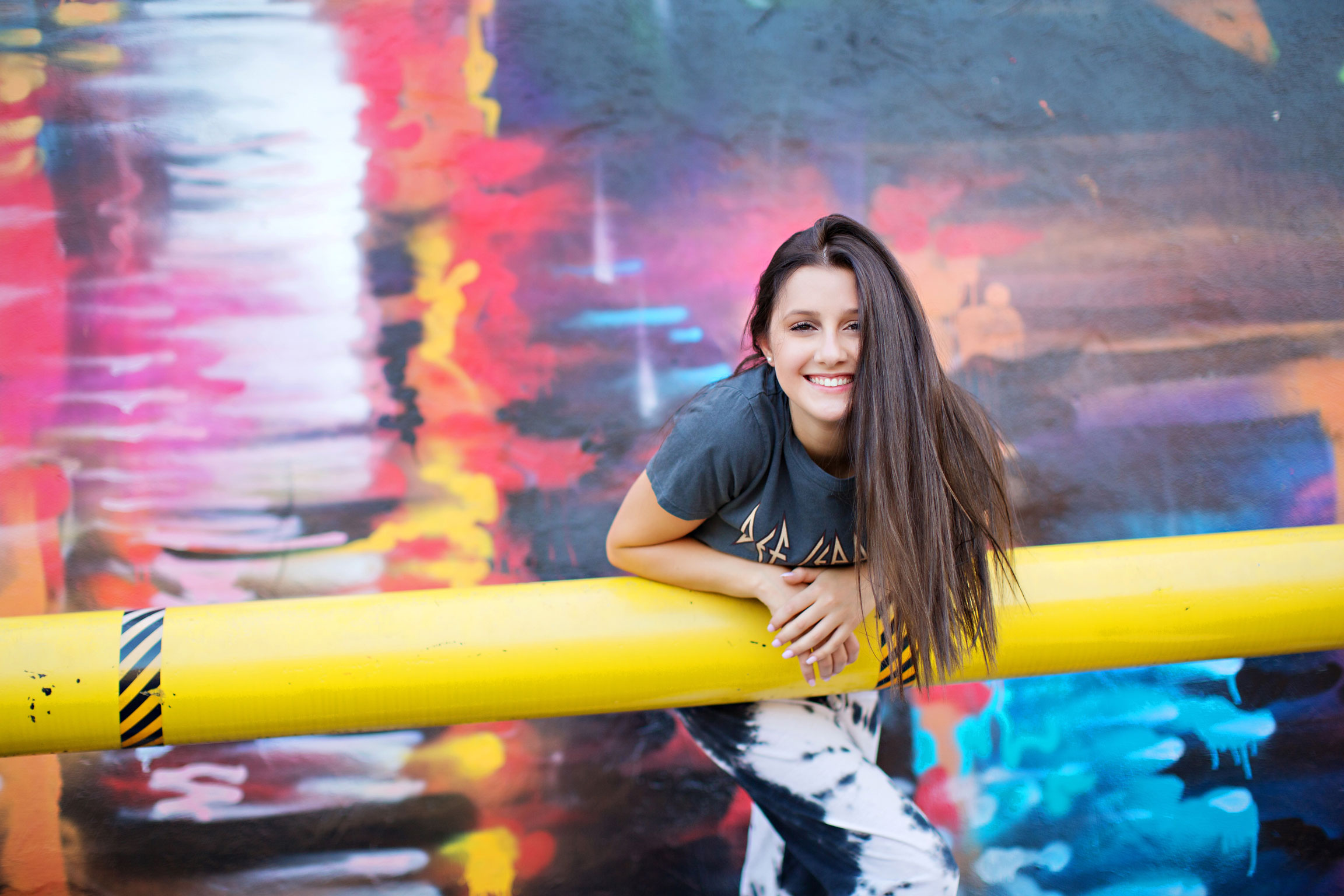 Smiling girl leaning against yellow rail with mural background